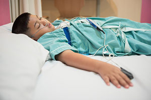 This is a picture of a little boy laying on a hospital bed with wires hooked up to him